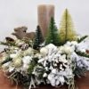 Stroik dekoracja świąteczna ośnieżona zachowana w leśnym rustykalnym klimacie udekorowana świecą , drewnianym łosiem i małymi choinkami ubrana ośnieżony stroik bożonarodzeniowy oryginalny nowoczesny