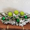 Stroik dekoracja bożonarodzeniowa obsypana puchatym białym śniegiem z zielonymi świecami i srebrno zielonymi dekoracjami nowoczesna ozdoba świąeczna kolor zielony ośnieżona ubrana udekorowana unikatowa