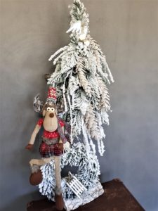 Piękna choinka ze stroikiem ośnieżona na biało z siedzącym dużym świątecznym reniferem na wianku