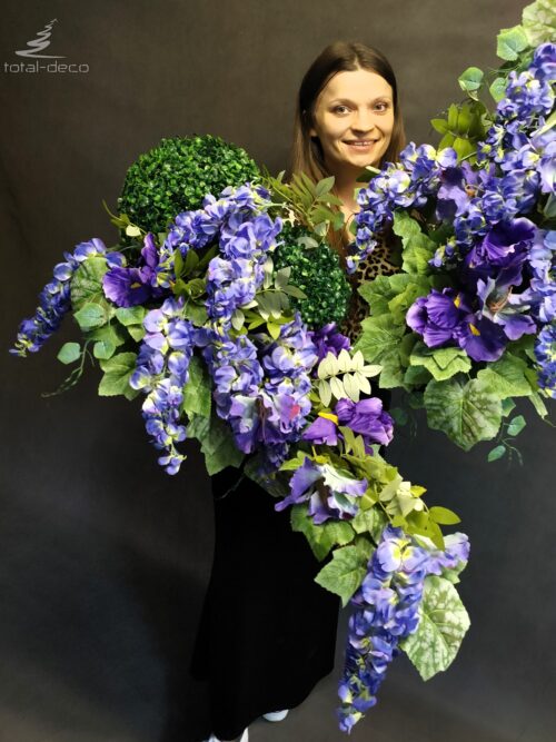 Kompozycje cmentarne "Kaskada Wisterii" z eleganckimi kwiatami wisterii i zielonym bukszpanem, osadzonymi na naturalnej polanie z brzozy.